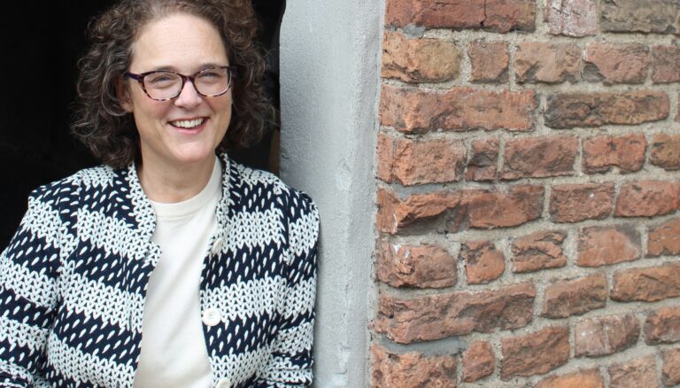 Miranda leunt tegen een muur in Deventer en kijkt lachend de camera in.